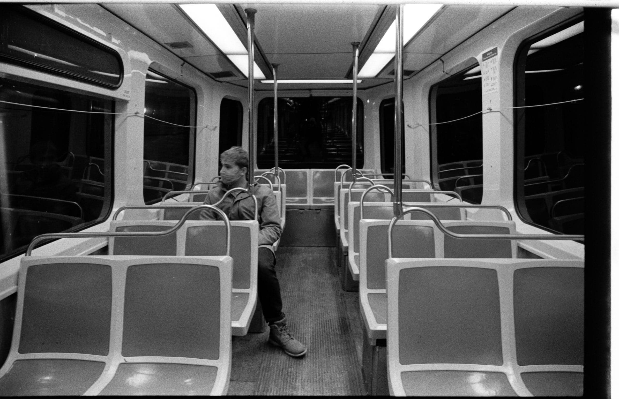 Interior of an empty public transit vehicle with rows of seats, with one person standing near the doors.